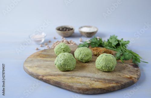 raw falafel balls of chickpeas, herbs and spices with ingredients for cooking on a wooden cutting board on a light wooden background. Vegetarian healthy food The concept of healthy eating  Copy  space