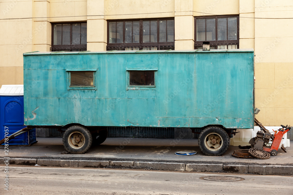 green construction trailer on wheels stands on a repaired street. replacement of urban communications and updating of the road surface green construction trailer on wheels stands on a repaired street. replacement of urban communications and updating of the road surface