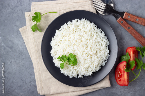 Фотография Steamed rice on black plate. Gray stone background. Top view.