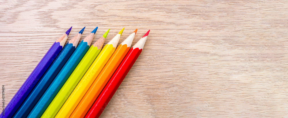 Fototapeta premium Different colored pencils photo with space for text. Seven pencils of rainbow colors lie on the table. Copyspace. Back to school. Wooden background.