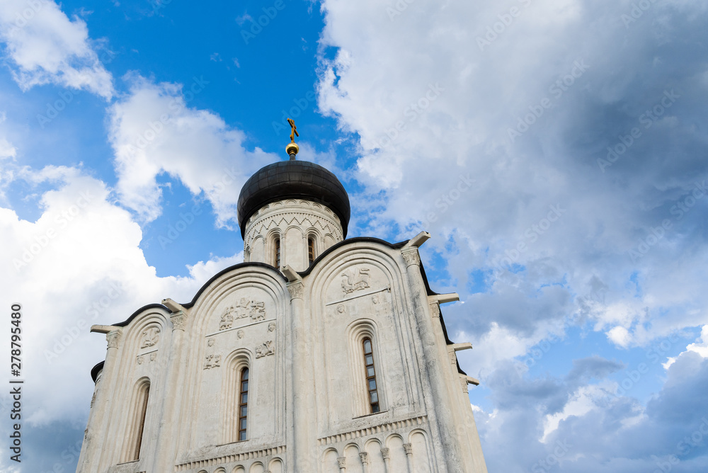 Fototapeta premium Orthodox church on a green meadow with trees and blue cloudy sky