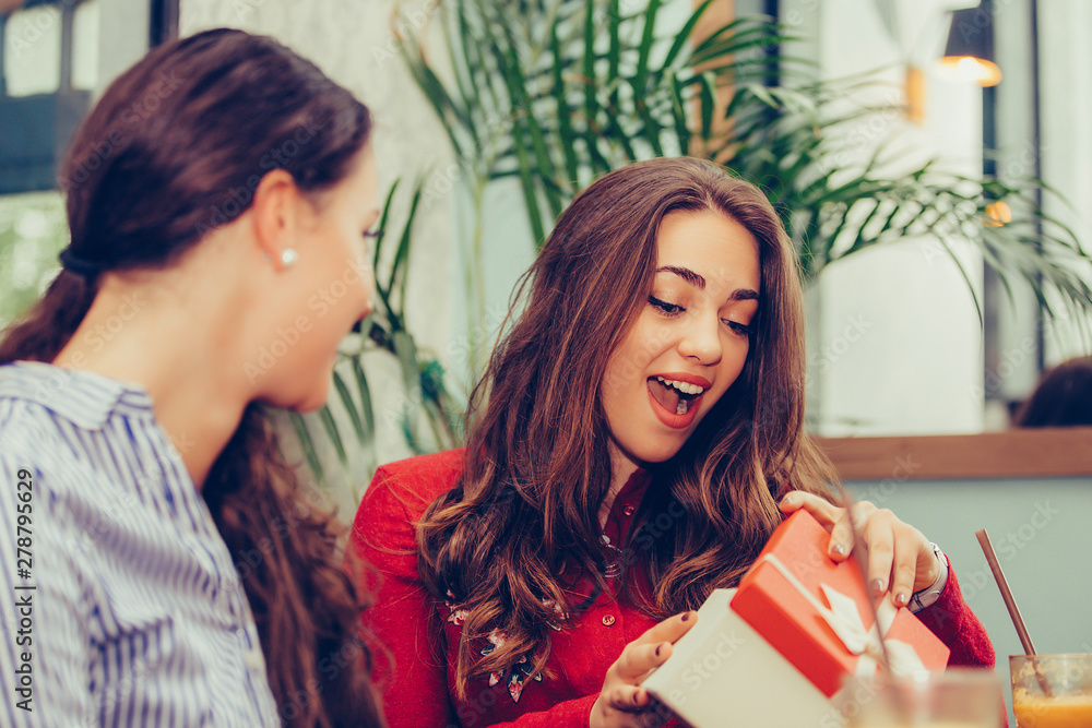 Beautiful girl sitting in cafe with her friend and receiving a gift Beautiful girl sitting in cafe with her friend and receiving a gift