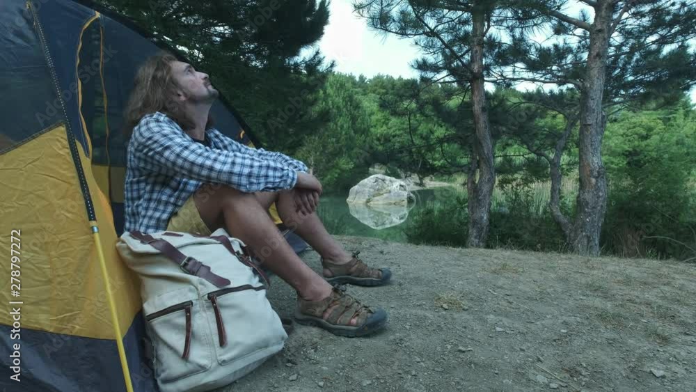 Spring holiday, hike travelling with camp and friends. Scene of spring morning outdoor, man looks at the sky sitting in tent, smile thinking about holiday. Friendship concept and trip around the world Spring holiday, hike travelling with camp and friends. Scene of spring morning outdoor, man looks at the sky sitting in tent, smile thinking about holiday. Friendship concept and trip around the world