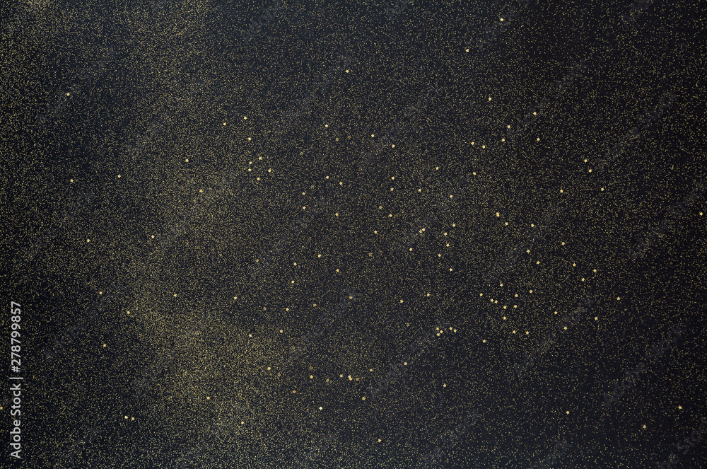 Golden glitter and stars scattered on the black background. Black glitter texture Christmas abstract background. Top view, selective focus.  