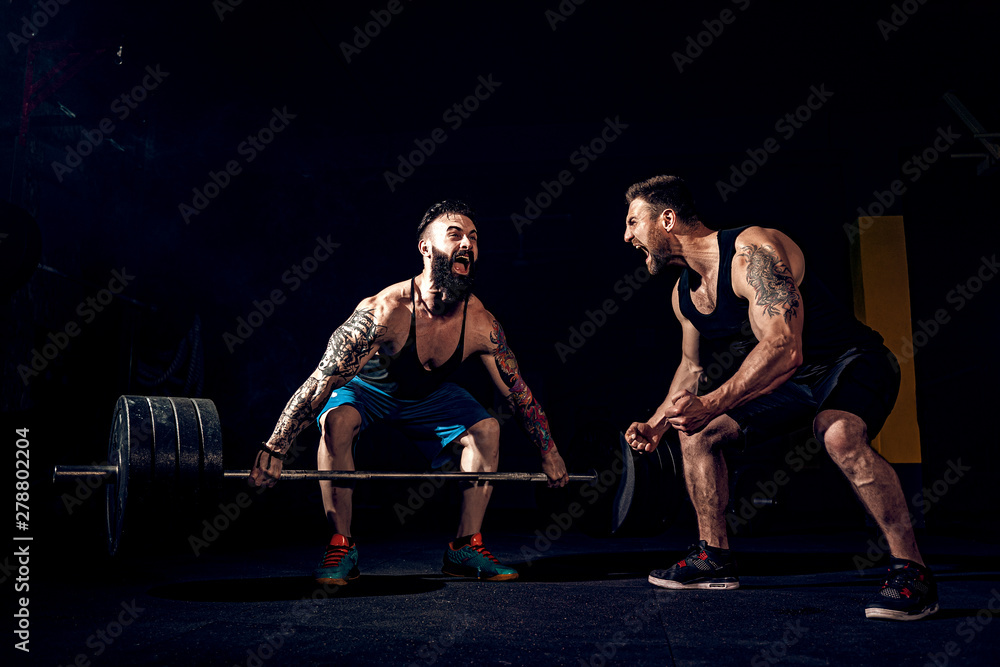 Two muscular bearded tattoed athletes training, one lift heavy weight ...