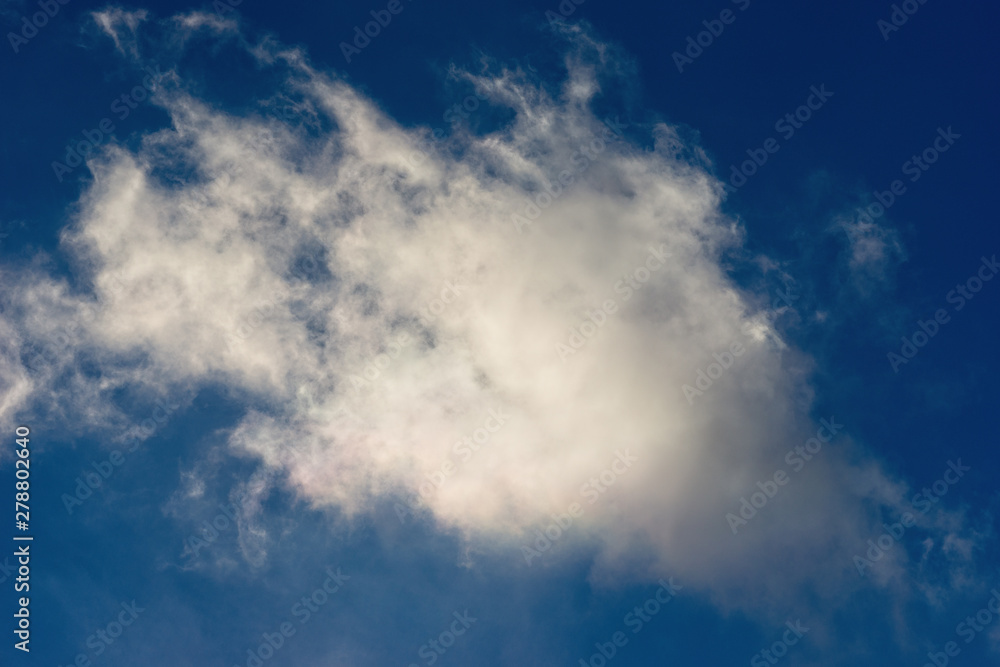 Sunlit white cloud against the background of dark blue sky. Fresh atmosphere, natural light