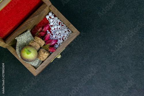 Close up view of scattered homeopathic pills with pink flowers, wild fruit, bottle’s cork and burlap in wooden old box on dark background. Homeopathic Medicine concept photo