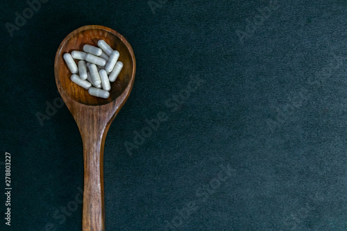 Herbal capsules in wood spoon on dark background. Natural medicine concept