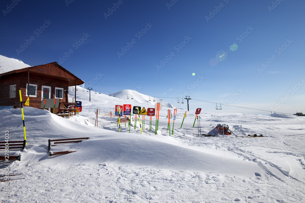 High snowy mountains, wooden rescue house, warning signs in snowdrift