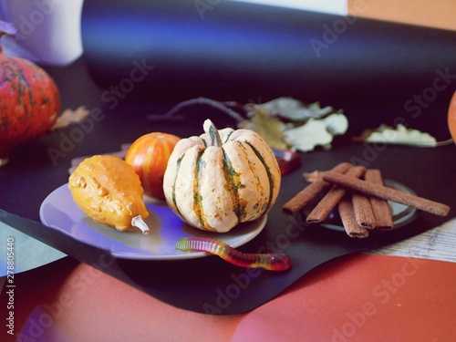 Decorative composition of pumpkins, leaves, chocolate cookies, jelly worms on a bright background, illuminated with blue light, on the table, Halloween, October