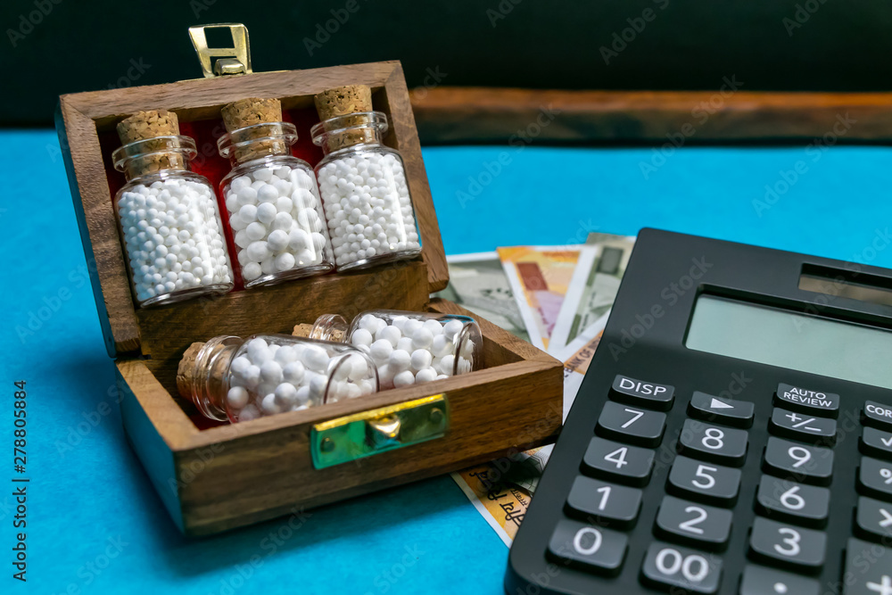 Wooden box with homeopathic medicine glass bottles and calculator, Indian rupees on blue and dark background - Money and Medicine concept