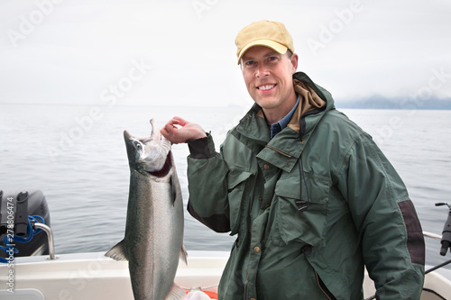 Smiling fisherman in Alaska holds up nice silver salmon photo