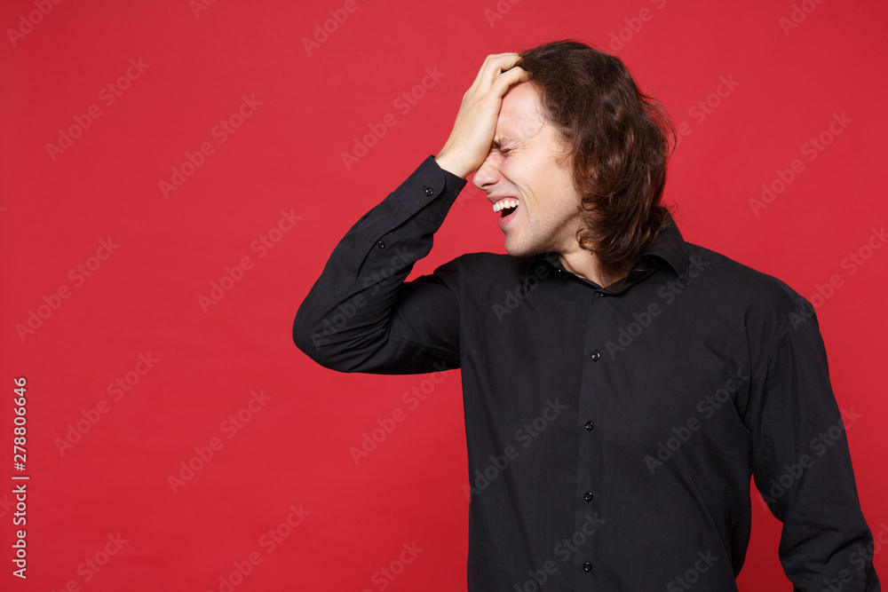 Young sad curly long haired man in black shirt standing posing isolated on red wall background studio portrait. People sincere emotions lifestyle concept. Mock up copy space. Problem crisis depression Young sad curly long haired man in black shirt standing posing isolated on red wall background studio portrait. People sincere emotions lifestyle concept. Mock up copy space. Problem crisis depression