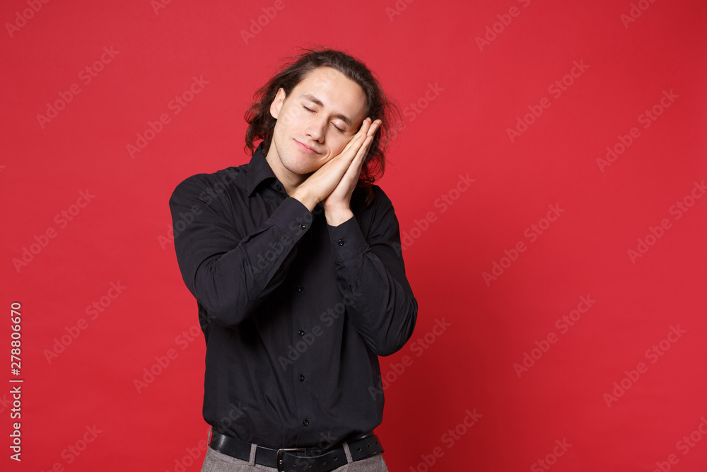 Young curly long haired man in black shirt posing isolated on red wall background studio portrait. People sincere emotions lifestyle concept. Mock up copy space. sleep with folded hands under cheek. Young curly long haired man in black shirt posing isolated on red wall background studio portrait. People sincere emotions lifestyle concept. Mock up copy space. sleep with folded hands under cheek.