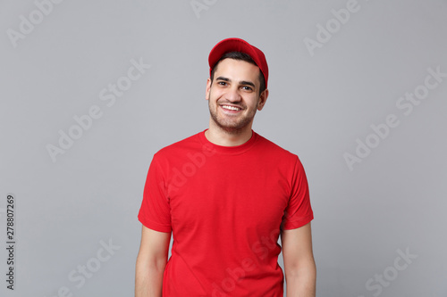 Delivery man in red uniform workwear isolated on grey wall background, studio portrait. Professional male employee in cap t-shirt print working as courier dealer. Service concept. Mock up copy space.