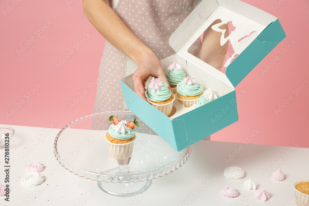 Φωτογραφία Close up cropped housewife female chef cook confectioner or baker in apron white t-shirt packaging cake cupcake at table isolated on pink pastel background in studio