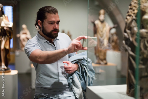 Bearded man photographs museum exhibits using smartphone
