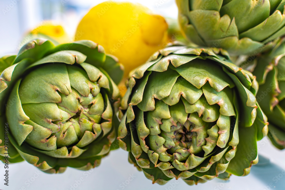 Fototapeta premium Heads flowers of fresh raw artichokes plants from artichoke plantation in Argolida, Greece ready to cook with lemon