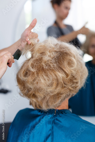 Hands of hairdresser making hairstyle for female