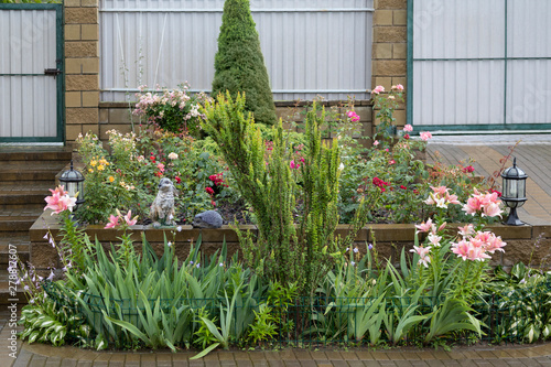 landscape design with a well-groomed flowerbed of roses and lilies with sculptures of a hare and a hedgehog and decorative lanterns after the rain