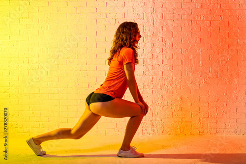 Young athletic woman doing lunges on a yellow background.