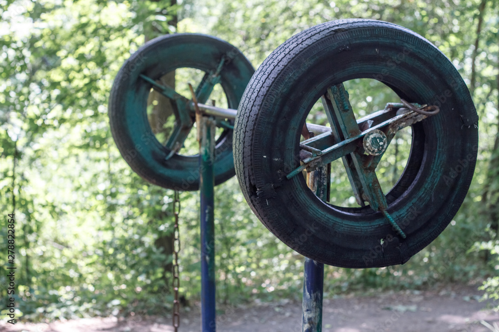 Close-up of a rough home-made simulator from old tires among thick trees in a city park, healthy lifestyle concept, selective focus