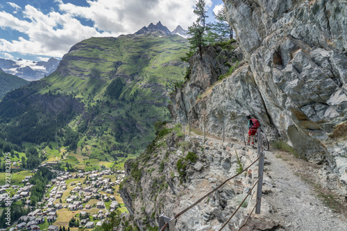 active senior woman, pushing her electric mountain bike on a narrow mountain bike trail high above Zermatt, the famous touristic destination in the swis alps, Canton Valais, Wallis, 