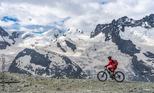 active senior woman, riding her electric mountainbikeon the Gornergrat in Zermatt, Wallis,Switzerland. In The background Gorner Glacier, Monte Rosa, Liskam am Breithorn