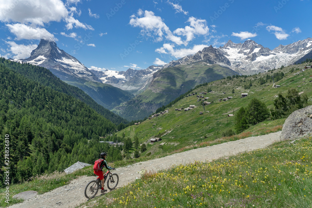 Fototapeta premium woman on mountain bike above the village of Findeln, high above of Zermatt, Vallais,Wallis, Switzerland, famous Mount Matterhorn in the background