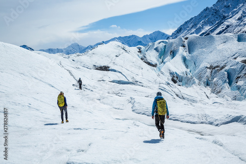 Three guides hiking up the Matanuska Glacier. Trekking on white ice of a valley glacier in remote Alaska.