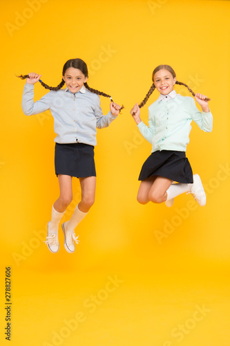 Beautify your hairstyle today. Adorable small girls with long hairstyle jumping on yellow background. Cute little children holding braided hairstyle in mid air. Great hairstyle every day