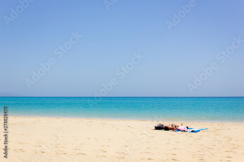 Lonely woman sunbathing on empty beach. Female tourist enjoying summer holidays on paradise island with turquoise water sea. Travel vacation, unique destination concepts