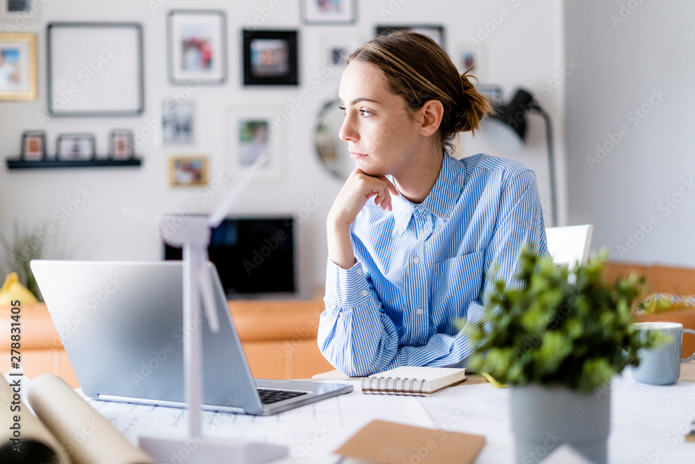 Woman in office looking sideways with wind turbine model on table Woman in office looking sideways with wind turbine model on table