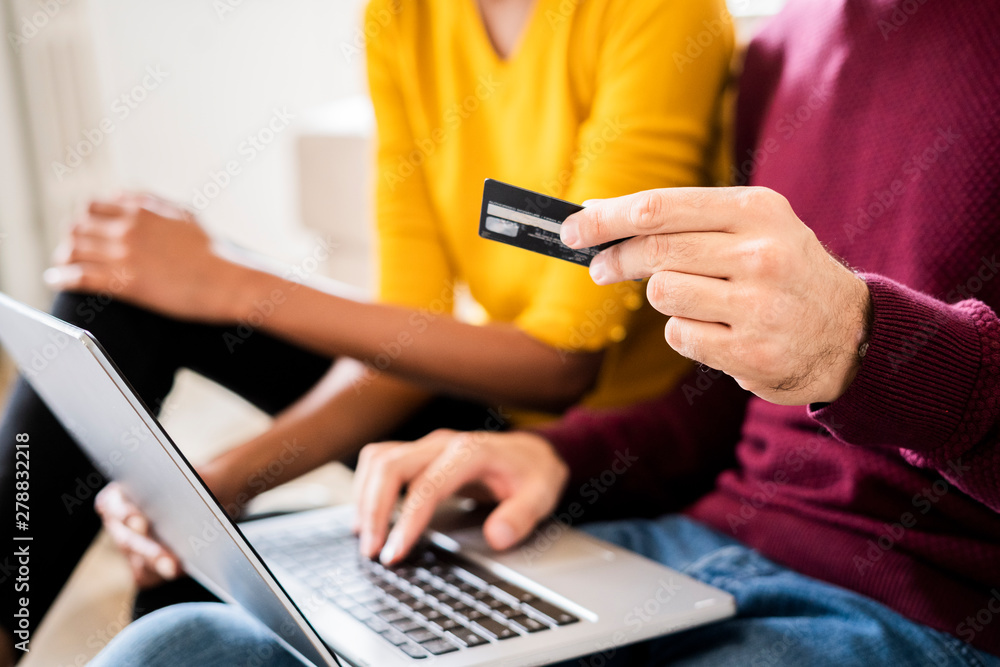 Close-up of couple at home shopping online with laptop and credit card Close-up of couple at home shopping online with laptop and credit card