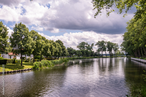 Sluis, the Netherlands - June 16, 2019: Reflecting water of canal to Damme in Belgium, with curtains of green trees on sides, under a storm approaching cloudscape.