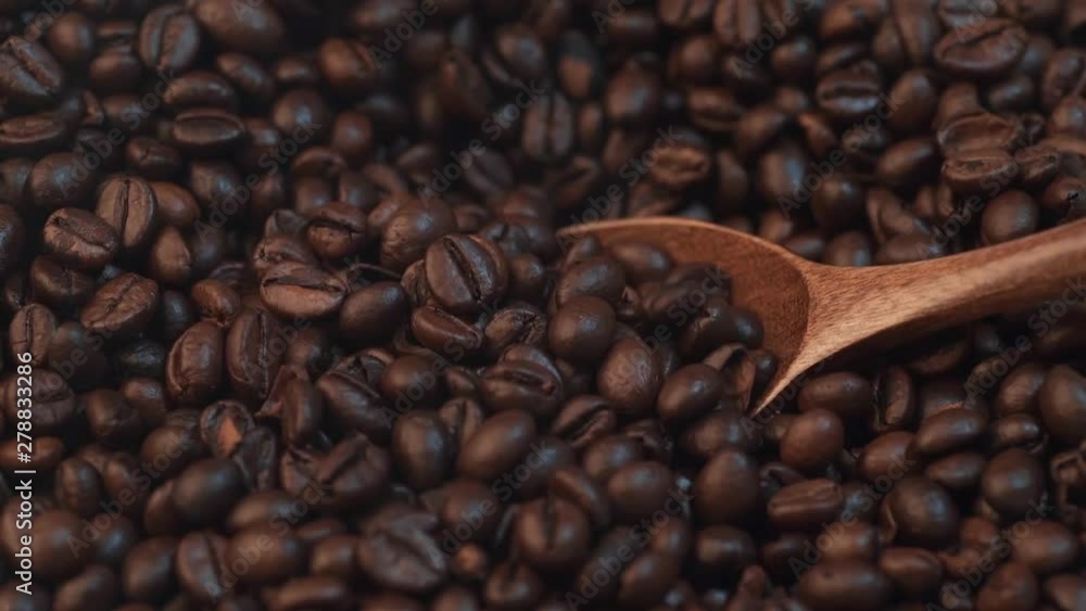 Roasted brown coffee beans mixed with wooden spoon, slow motion, macro shot Roasted brown coffee beans mixed with wooden spoon, slow motion, macro shot