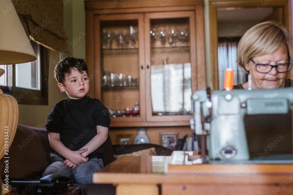 Grandmother using an old sewing machine watched by her grandson Grandmother using an old sewing machine watched by her grandson