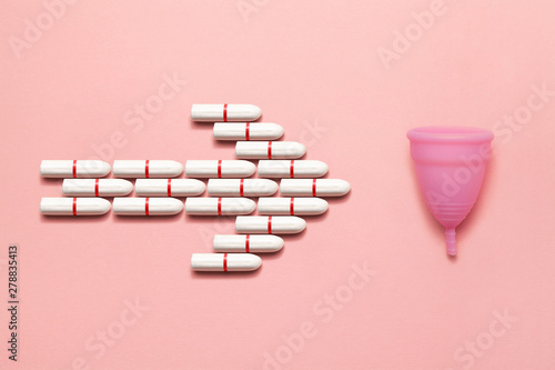 Reusable silicone menstrual cup and heap of tampons comparison on a soft pink background. Modern female intimate alternative gynecological hygiene. Go eco zero waste concept photo