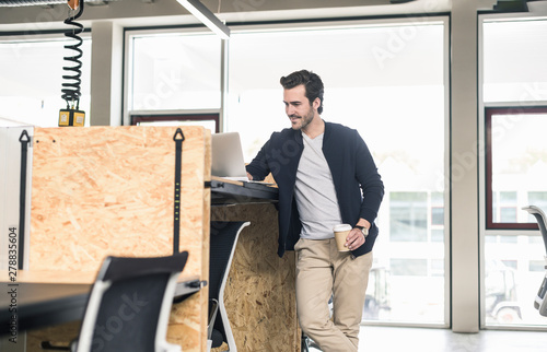 Young businessman in modern office, using laptop on high desk photo