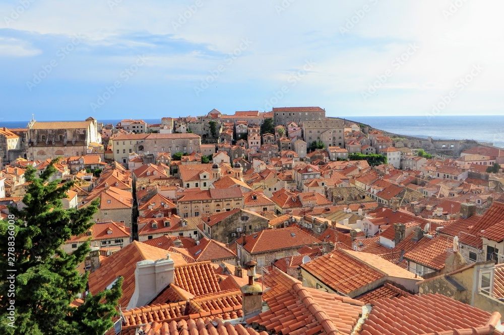 A full view of the old town in Dubronvik Croatia from the perspective of the walls of Dubronvik. The old town is all old homes with clay tiled roofs and the beautiful adriatic sea is in the background