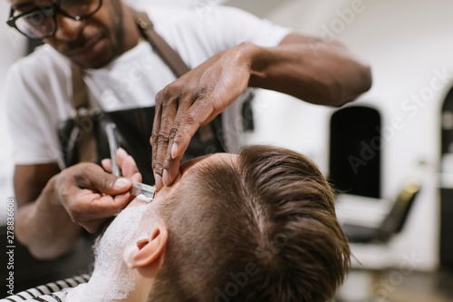 Man getting his beard shaved with razor in barber shop