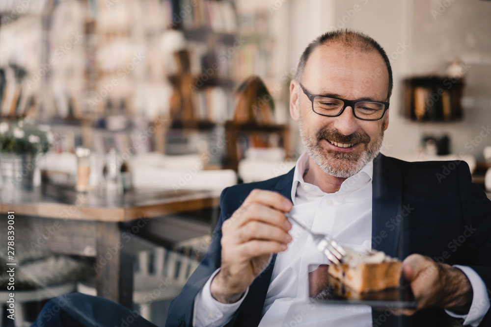 Mature businessman having a piece of cake on a digital tablet in a cafe Mature businessman having a piece of cake on a digital tablet in a cafe