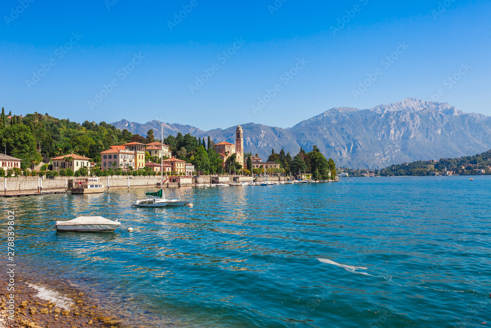 Fototapeta premium Panorama landscape on beatiful Lake Como in Tremezzina, Lombardy, Italy. Scenic small town with traditional houses and clear blue water. Summer tourist vacation on rich resort with nice harbour