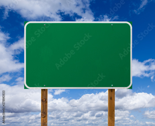 Blank Green Road Sign with Wooden Posts Over Blue Sky and Clouds