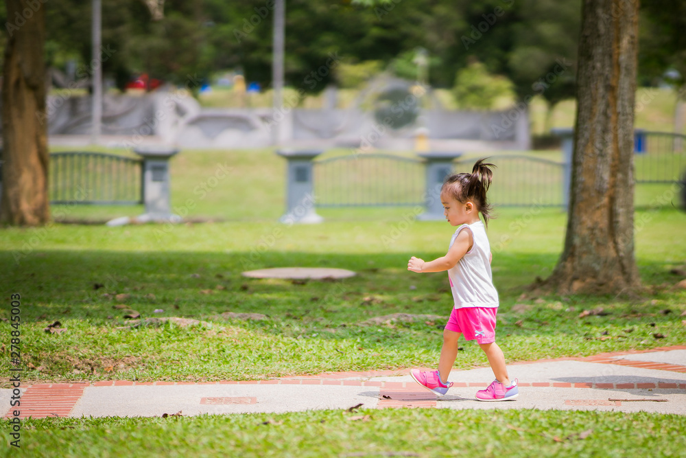Asian toddler girl running in the park at the spring or summer day.