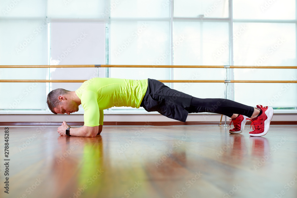 Plank it Confident muscled young man wearing sport wear and doing plank position while exercising on the floor in loft interior Plank it Confident muscled young man wearing sport wear and doing plank position while exercising on the floor in loft interior