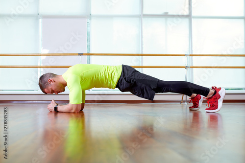 Plank it Confident muscled young man wearing sport wear and doing plank position while exercising on the floor in loft interior