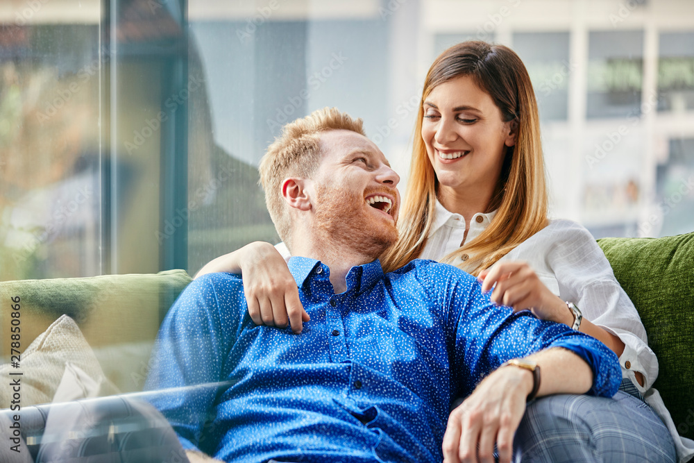 Happy couple sitting on couch, with arms around Happy couple sitting on couch, with arms around