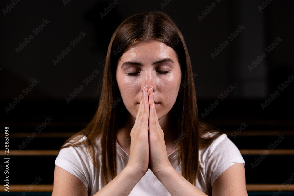 A Christian girl in white shirt is sitting and praying with humble heart in the church A Christian girl in white shirt is sitting and praying with humble heart in the church