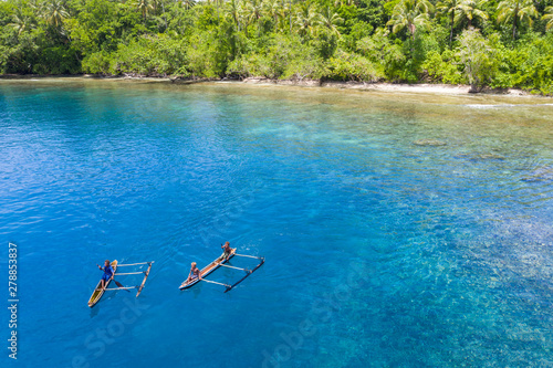 Villagers paddle their outrigger canoe in the warm, blue waters surrounding the island of New Britain in Papua New Guinea. This area is part of the Coral Triangle due to its high marine biodiversity. photo